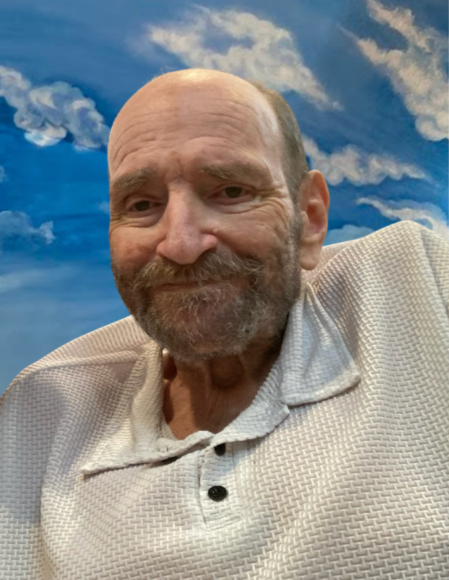 A photo of Guy, smiling. He is wearing a white polo shirt. The blue sky and white clouds evoking the Pure Land are painted on the temple wall behind him.